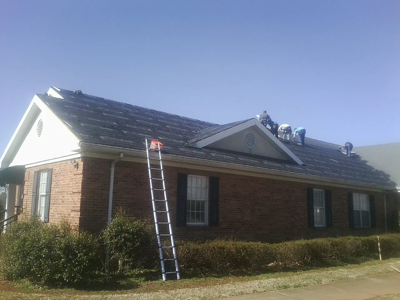 Crew tearing shingles off a brick ranch roof with a ladder set — Emergency Roof Repair work by our crew in Milledgeville