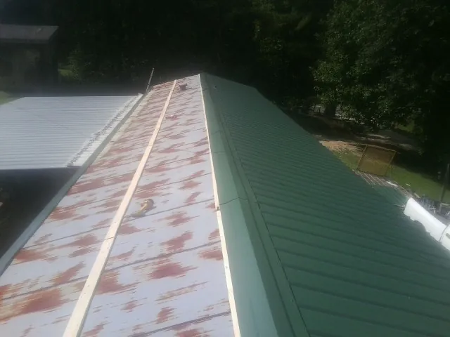 Old rusted panels beside newly installed green metal roofing — Wind Damage Roof Repair by Roofing Brothers in Milledgeville