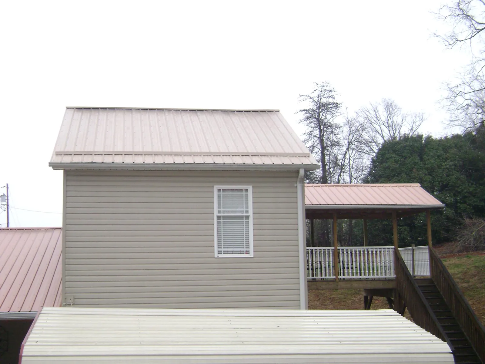 Tan metal roofs on a two story addition and attached porch, from a Roof Replacement job in Milledgeville